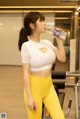 A woman in a white top and yellow leggings drinking water.