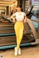 A woman standing in front of a treadmill in a gym.