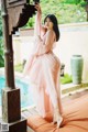 A woman in a pink dress standing next to a pool.