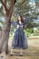 A woman leaning against a tree in a blue dress.