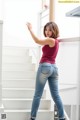 A woman in a red tank top and jeans standing on some stairs.