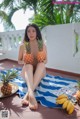 A woman sitting on a towel holding two pineapples.