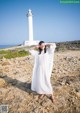 A woman in a white dress standing in front of a lighthouse.