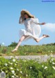 A woman in a white dress and straw hat jumping in the air.