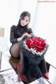 A woman sitting on a table holding a bouquet of red roses.