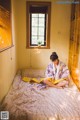 A woman in a kimono sitting on a bed in a room.