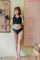 A woman in a black bikini standing in front of a wall.