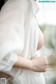 A woman in a white robe standing by a window.