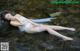 A woman in a white lingerie laying on a rock in a stream.