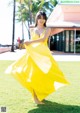 A woman in a yellow dress is dancing in the grass.