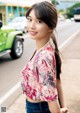 A woman standing on the side of a road next to a green car.