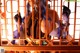 A woman with blue hair and a hat is standing behind bars.