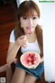 A young woman eating a slice of watermelon with a spoon.