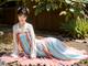 A woman in a blue and pink dress sitting on the ground.