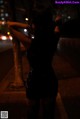 A woman in a black dress standing on a sidewalk at night.