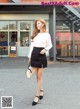 A woman in a white shirt and black skirt is walking down the street.