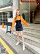 a woman in a black dress and orange sweater is walking down the street