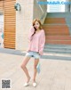 A woman in a pink sweater and denim shorts posing for a picture.