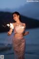 A woman in a pink dress holding sparklers on the beach.