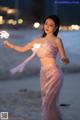 A woman in a pink dress holding a sparkler on the beach.