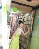 A woman in a green dress standing in front of a book shelf.