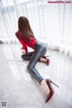 A woman in a red shirt and black leather pants crouching on the floor.