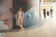 A naked woman standing in front of a large poster.