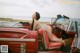 A woman sitting in the back of a red convertible car.