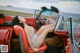 A woman sitting in the back seat of a red convertible car.