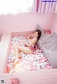 A woman laying in a bathtub filled with pink and white balloons.