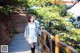 A woman in a white dress and fur coat standing on a wooden bridge.