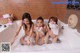 A group of three young women taking a bath in a bathtub.